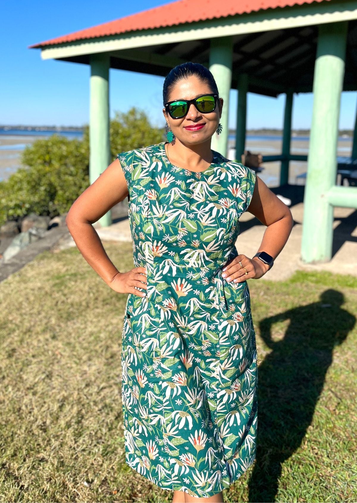 Woman wearing a cotton green floral dress standing outdoors near a gazebo.
