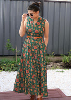 Woman wearing a cotton floral dress standing outdoors with a gray wall and plants in the background