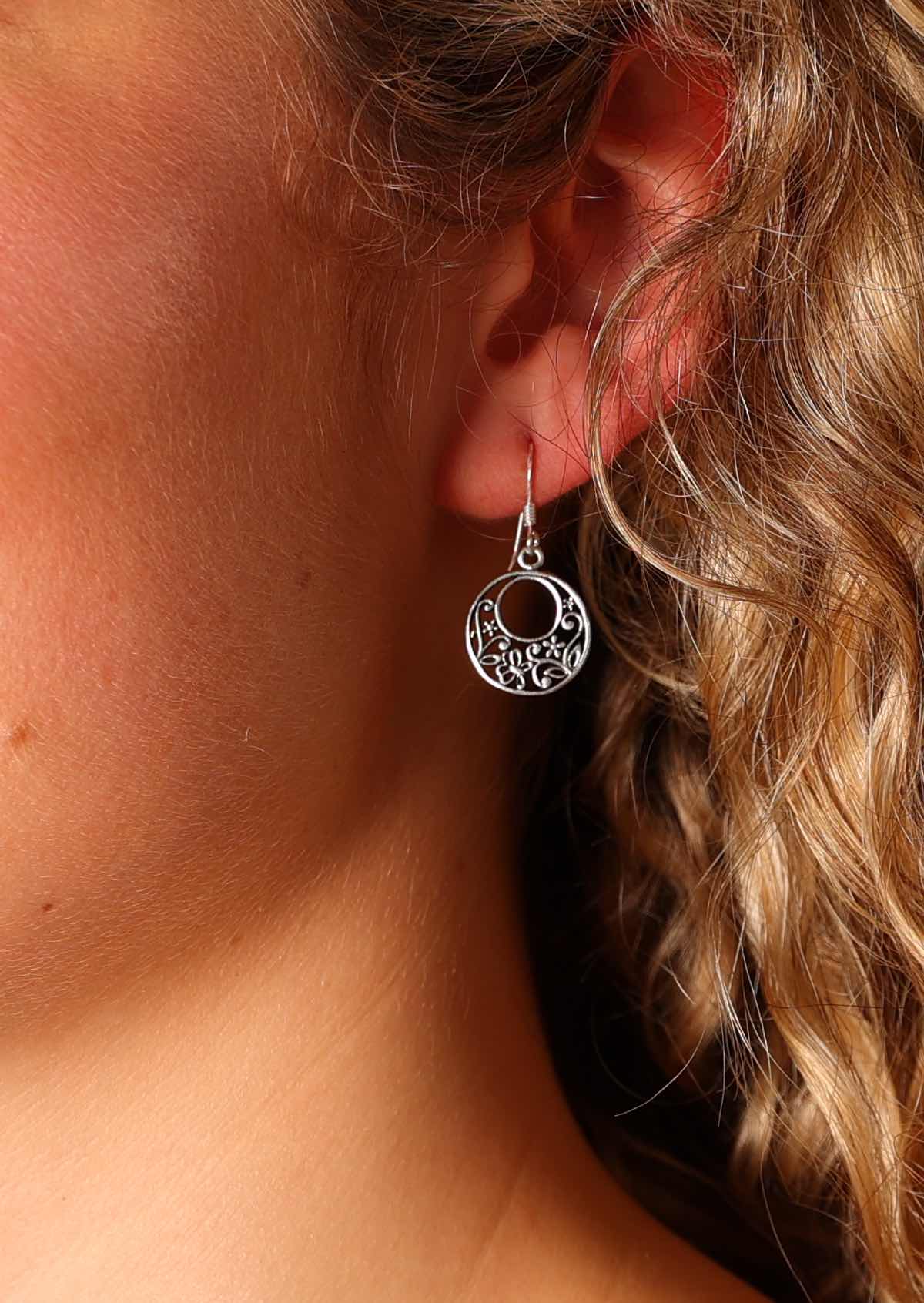 Crafted from sterling silver, these circular earrings feature an offset cutout hole and sweet floral detail in between the concentric circles