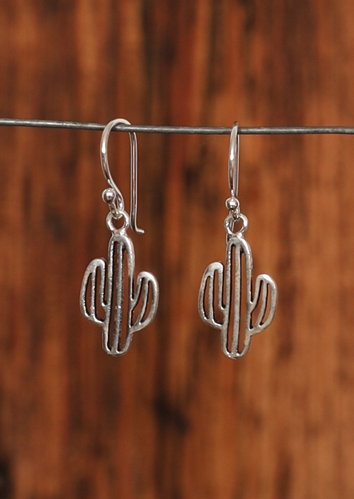 Sterling silver cutout cactus earrings suspended from wire hook.