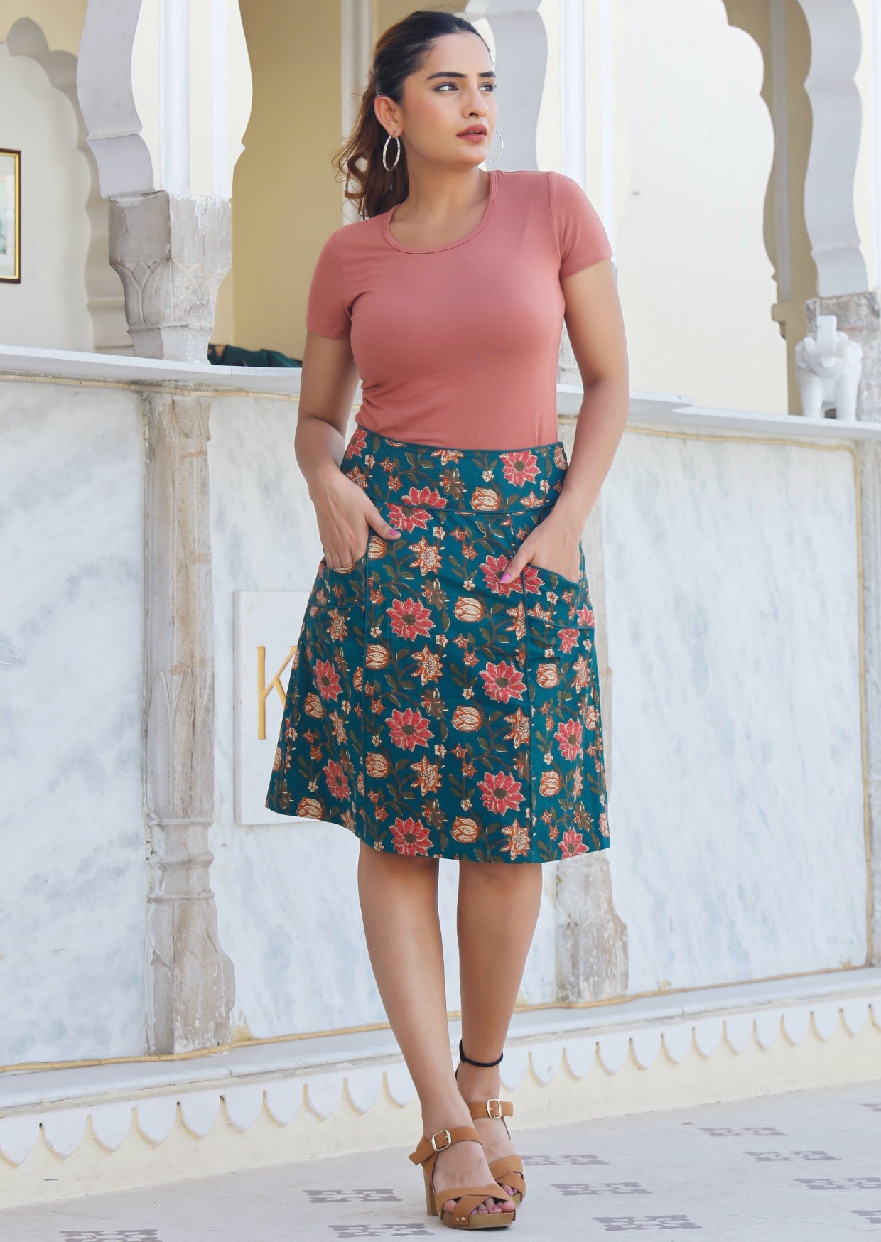 Model wears cotton A-line skirt in green based floral print with piped detail, paired with a dusty rose basic rayon top.