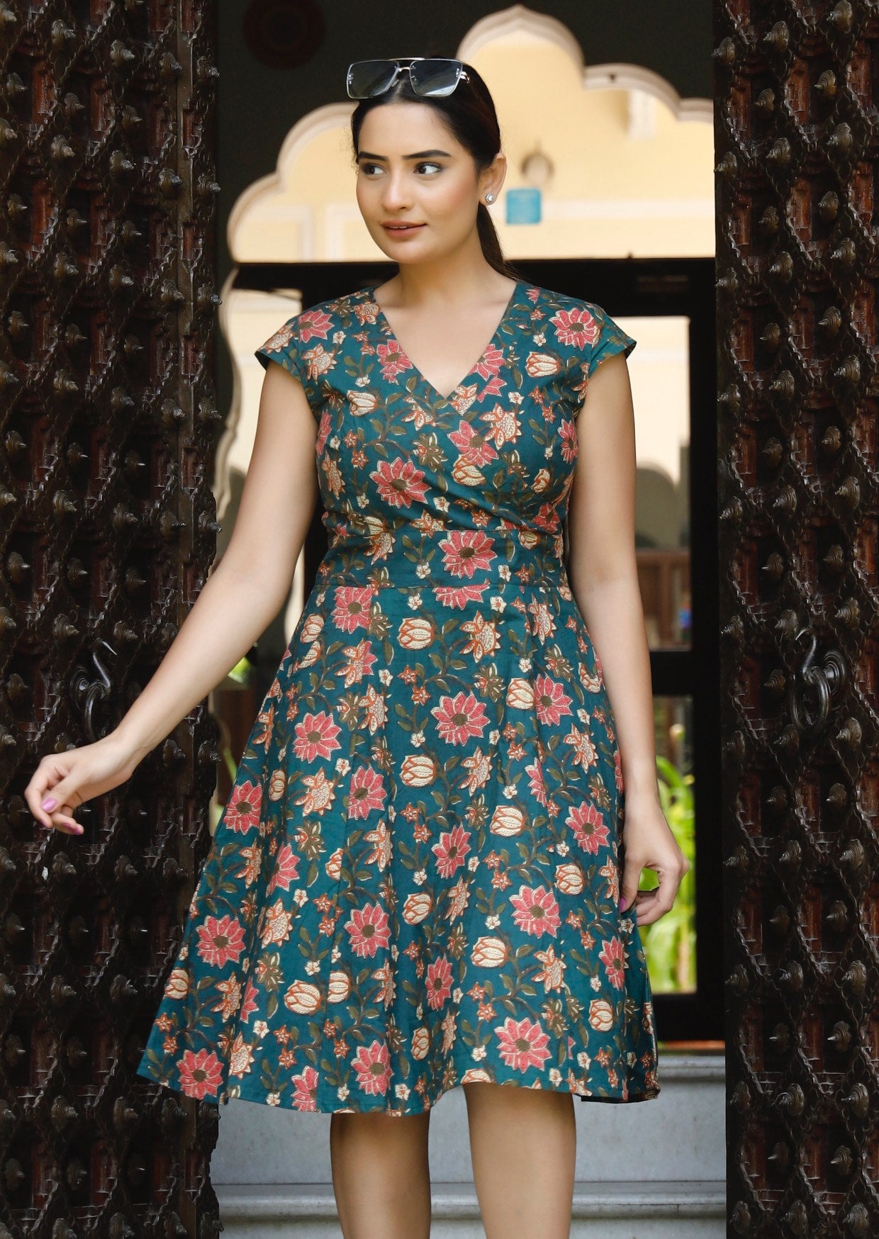 Woman poses in retro inspired cotton knee length dress in in green based floral print with cap sleeves and V neckline