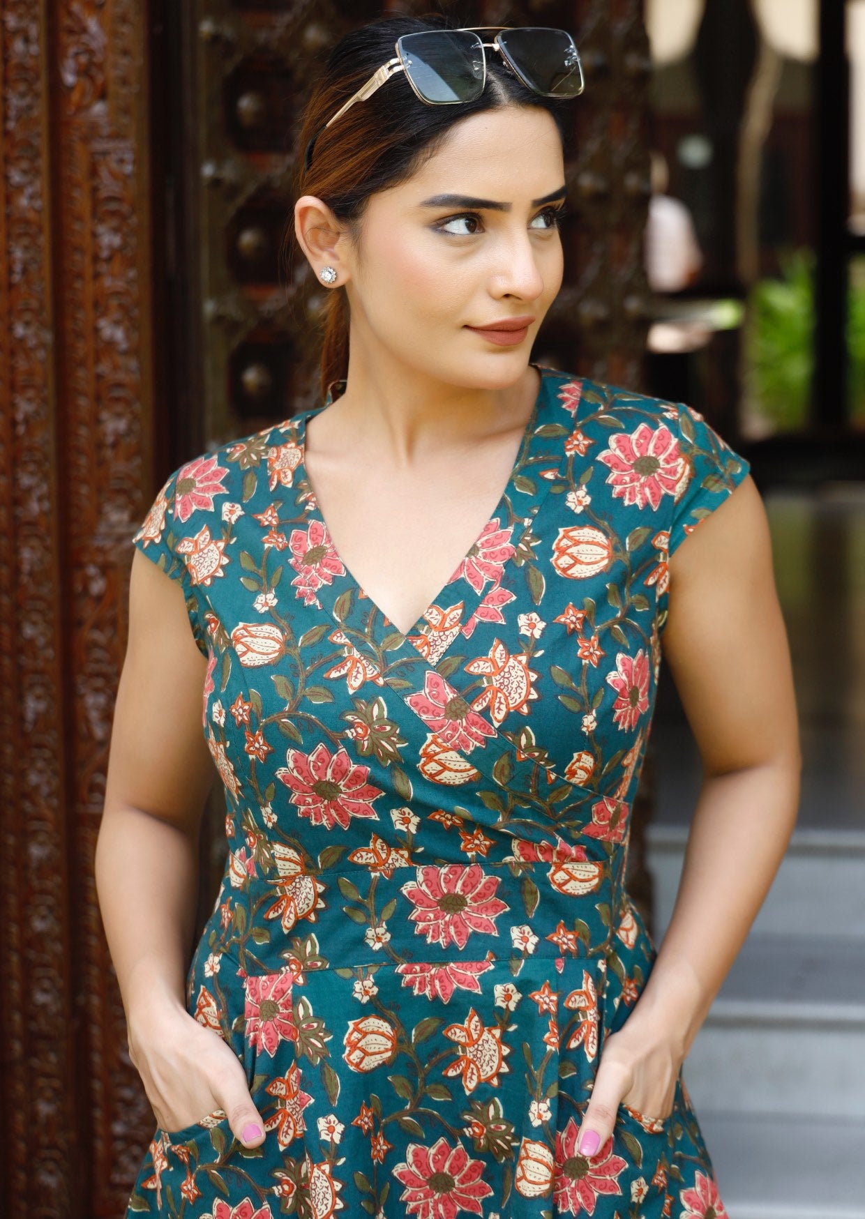 Zoomed in look of model wearing retro style cotton dress with crossover bodice and cap sleeves in pinkish floral print on deep green base.