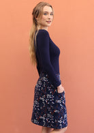 model wearing a mid length skirt featuring  a meadow flower print with blue, white and orange on a navy blue base.