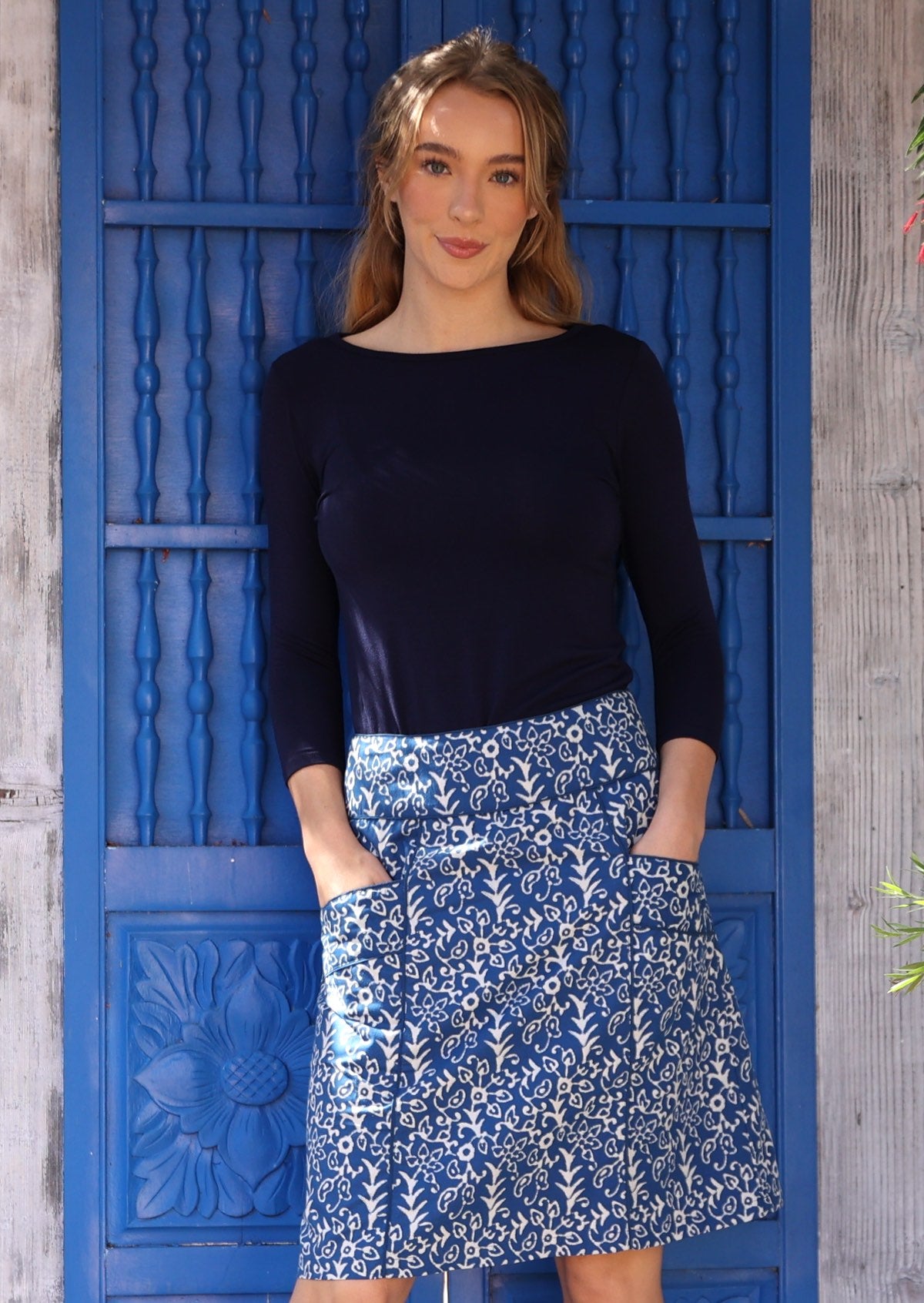 Model poses in cotton A-line above knee skirt with hands in deep pockets, paired with a dark blue 3/4 sleeve stretch rayon top