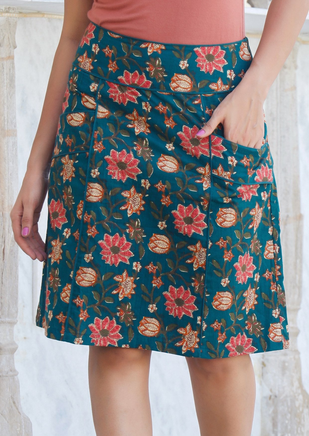 Model wears 100% cotton, above knee length skirt with piped details in sweet burgundy floral print on deep green base.