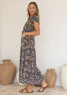 Woman wearing a floral maxi dress standing side on, with hands in pockets