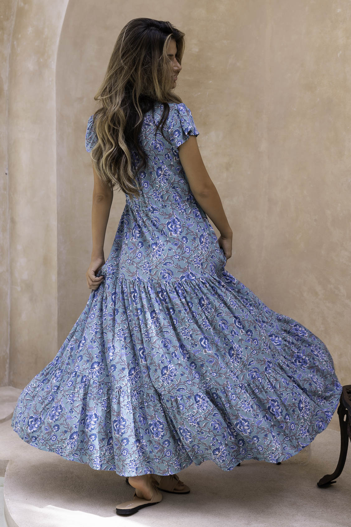 Woman wearing a floral maxi dress against a beige wall.
