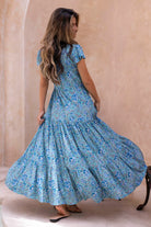 Woman wearing a floral maxi dress against a beige wall.