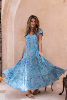 Woman in a beautiful blue floral maxi dress standing against a beige wall.