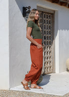 Woman standing with hands in pockets of brick orange wide-leg cotton pants with cuffed ankles and elasticated back waist