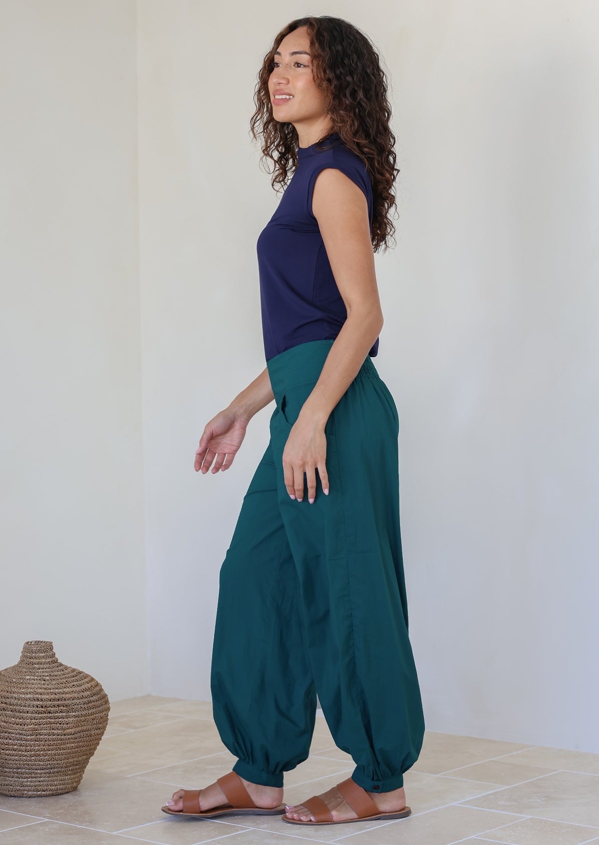 Side pose of model wearing 100% cotton wide leg pants in deep teal with pockets, cuffed ankles and shirred back waist
