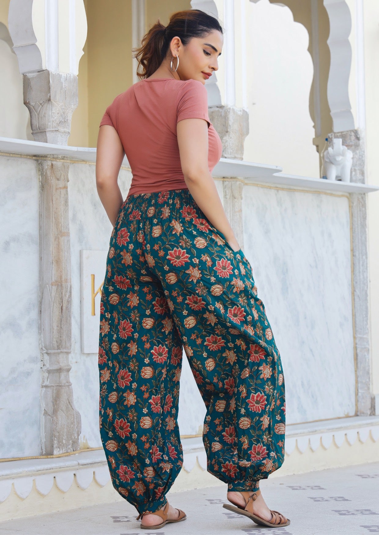 Model showcasing back of boho style cotton pants with hands in pocket, cuffed ankles with buttons and shirring across the back.