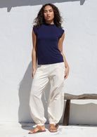 Woman wearing a navy top paired with genie style white cotton pants featuring deep pockets, a wide flat front waist and elastic at the back