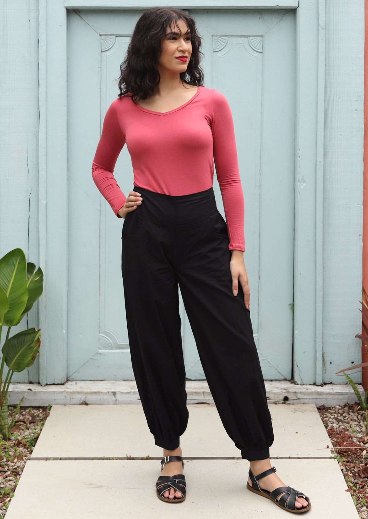 Woman wears black cotton pants with buttoned ankle cuffs paired with a long sleeve pink top