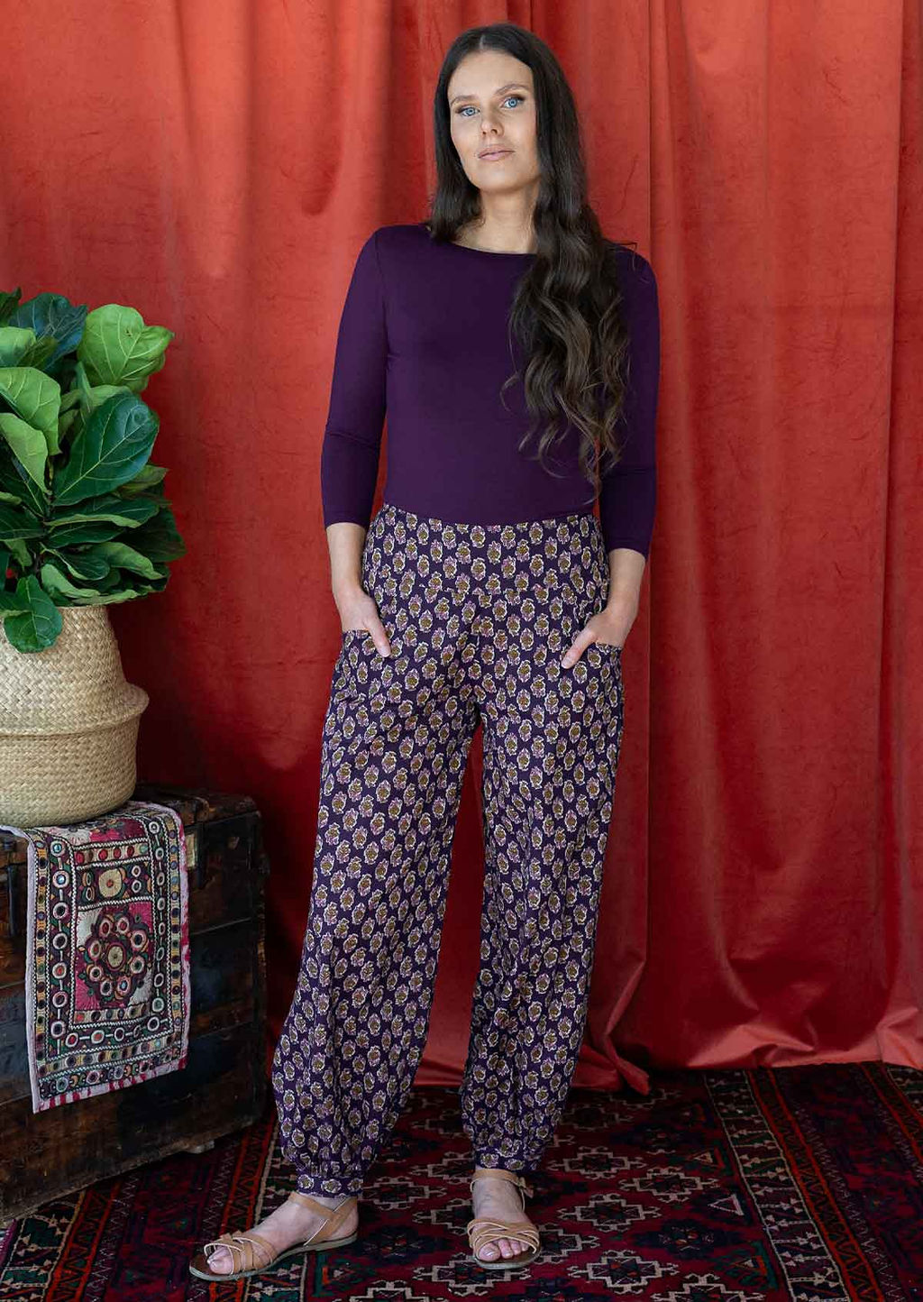 Woman wears cotton floral print harem pants with a wide waistband, with hands in pockets