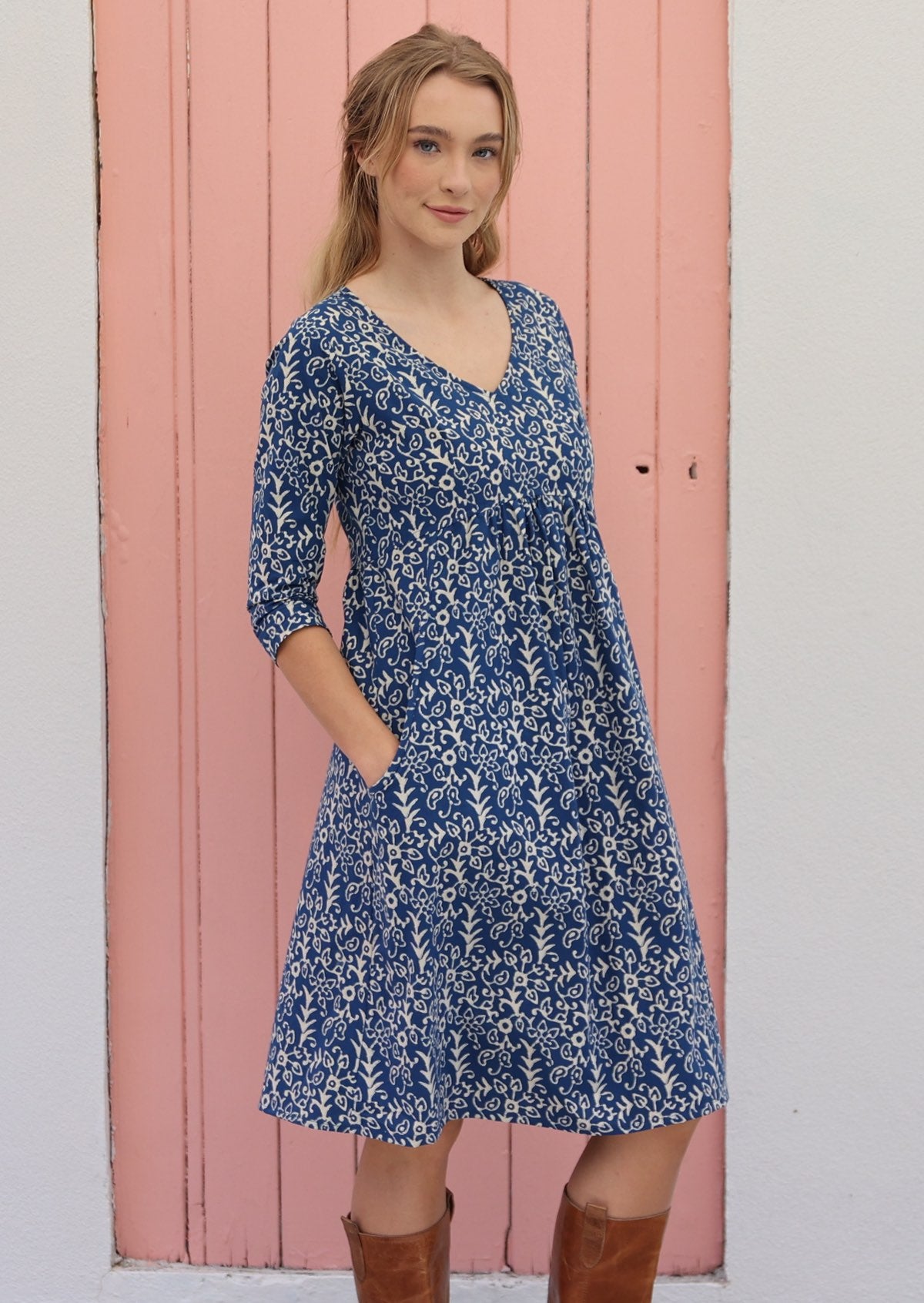 Woman wears cotton 3/4 sleeve dress with V-neckline and small gathers under the bust, with hands in pockets