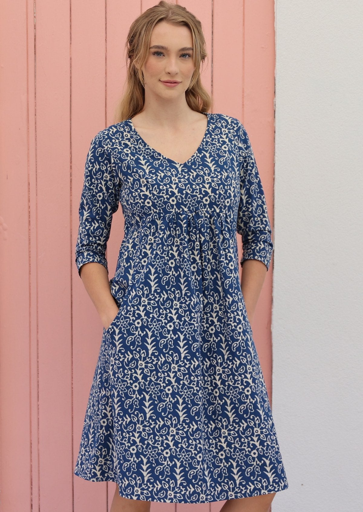Woman wears cotton over the knee length dress with 3/4 sleeves, V-neckline and pockets