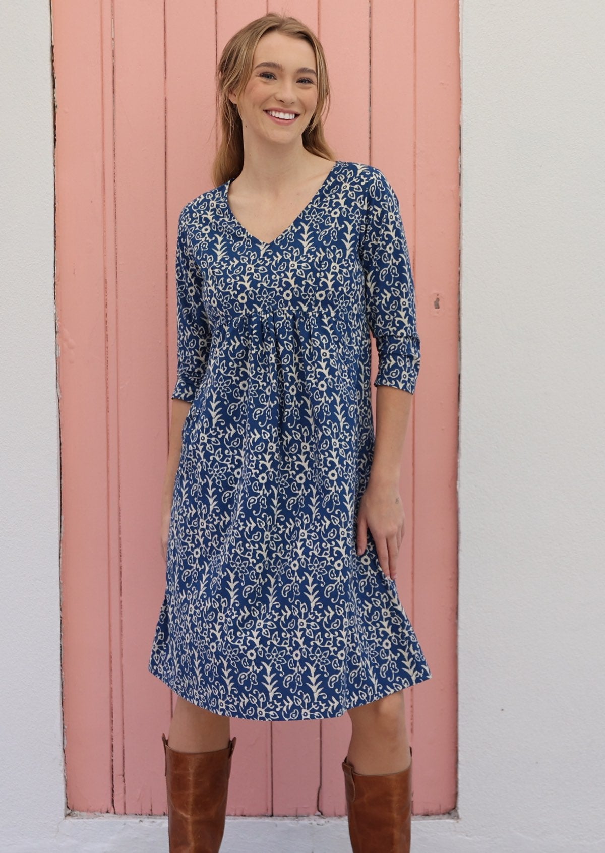 Model poses in cotton over the knee length dress with empire waistline and V-neck, in blue based floral print