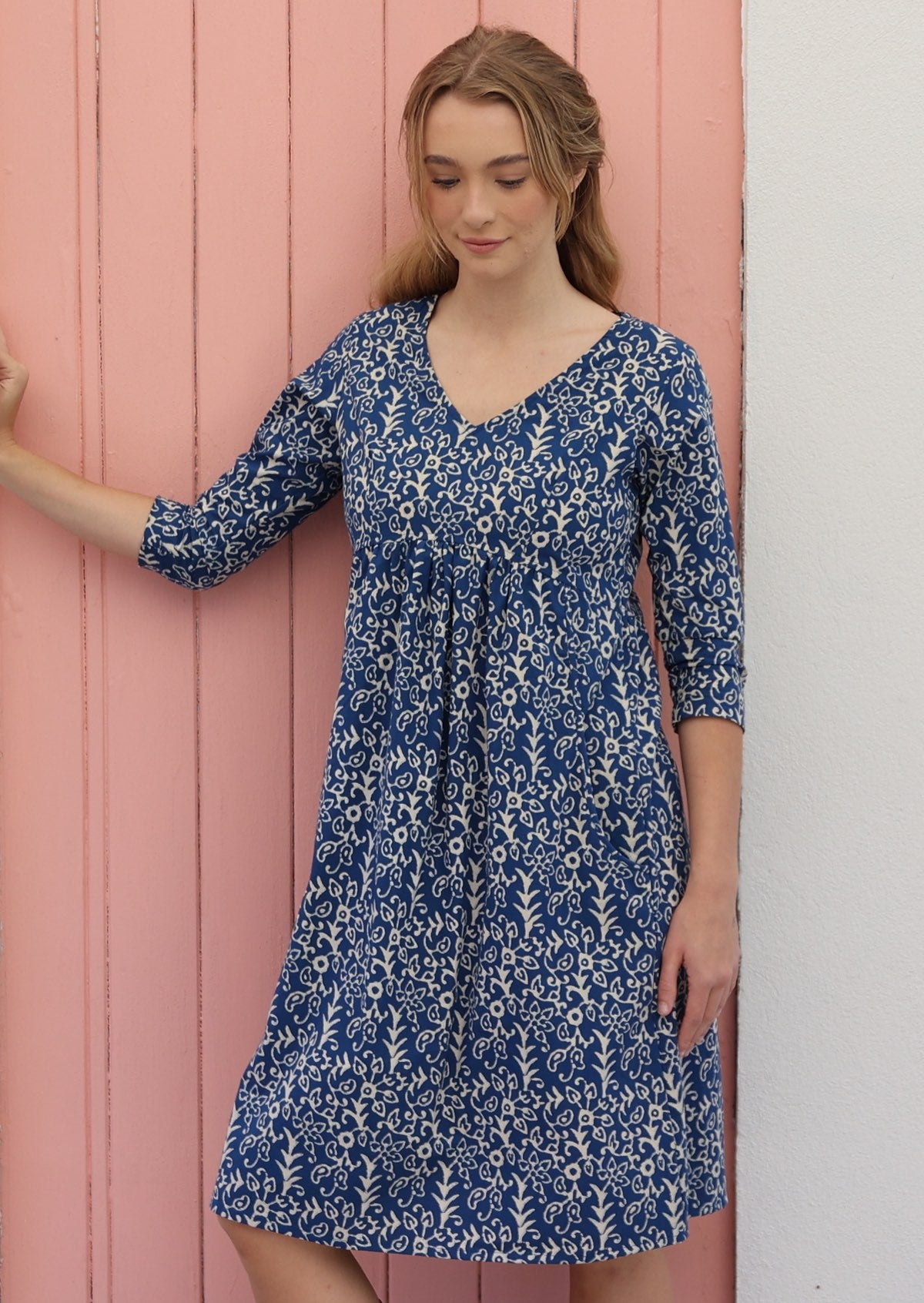 Woman wears cotton over the knee length dress with 3/4 sleeves, V-neckline and empire waistline