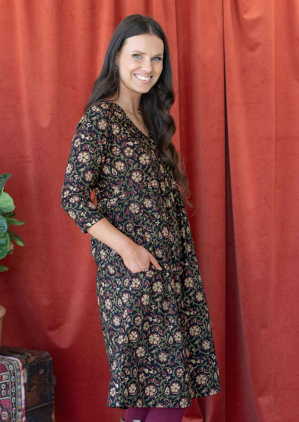 Woman wears cotton 3/4 sleeve black based floral print dress with a V-neckline, with her hands in pockets
