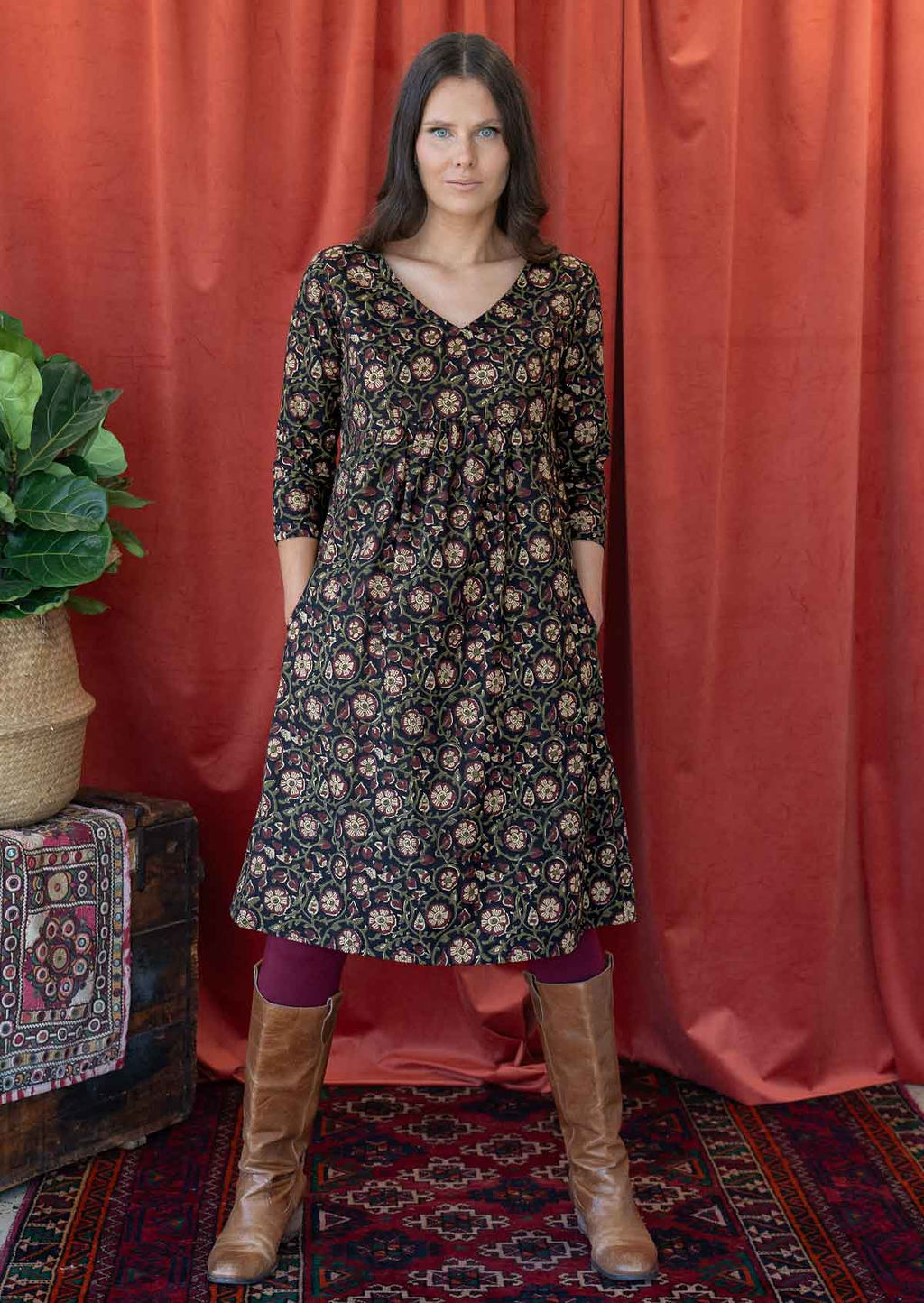Woman poses in cotton 3/4 sleeve black based floral print dress with a V-neckline and small gathers under the bust, with her hands in pockets