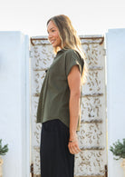 Woman stands in a side pose wearing a relaxed fit cotton collared top with short sleeves and V neckline