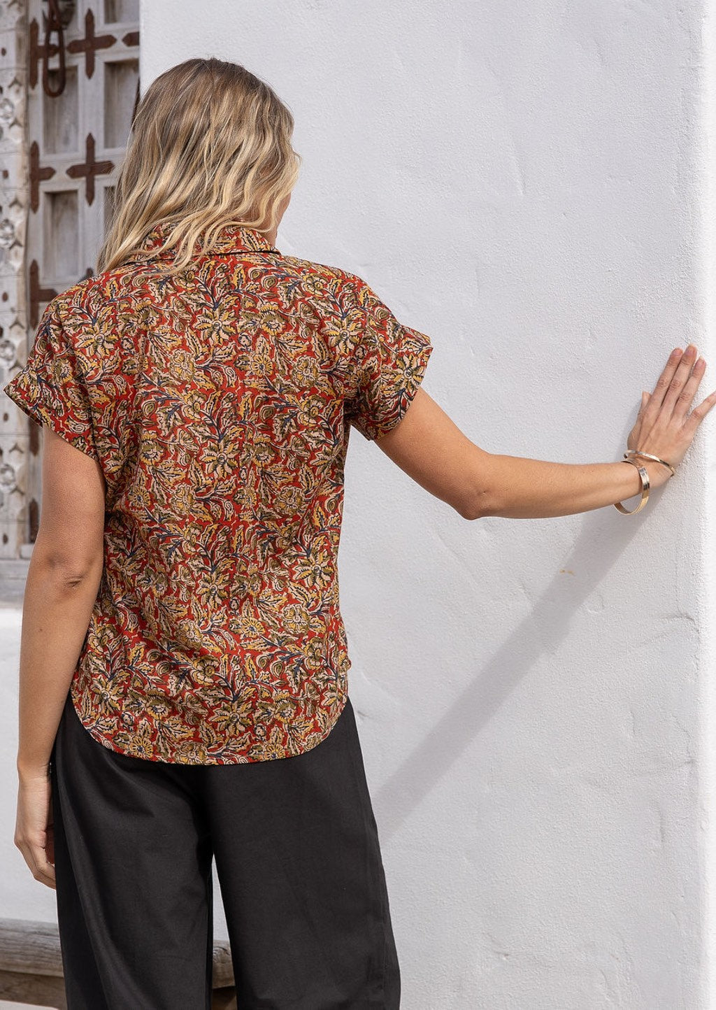 Back view of woman wearing an earthy toned cotton short sleeve shirt paired with black pants