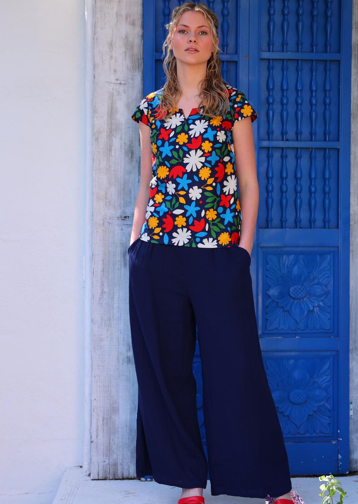 Model poses in cotton cap sleeved tailored top in fun bold print with hands in pockets of cotton pants
