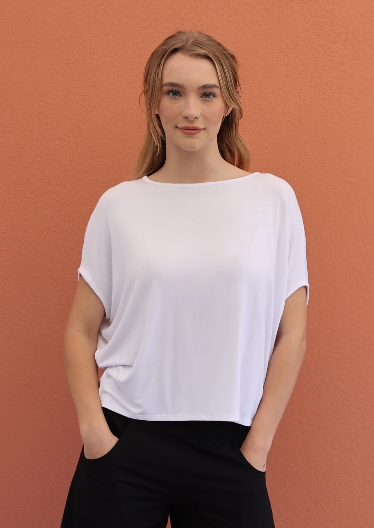 Woman wears white batwing t-shirt with boat neckline, paired with black pants