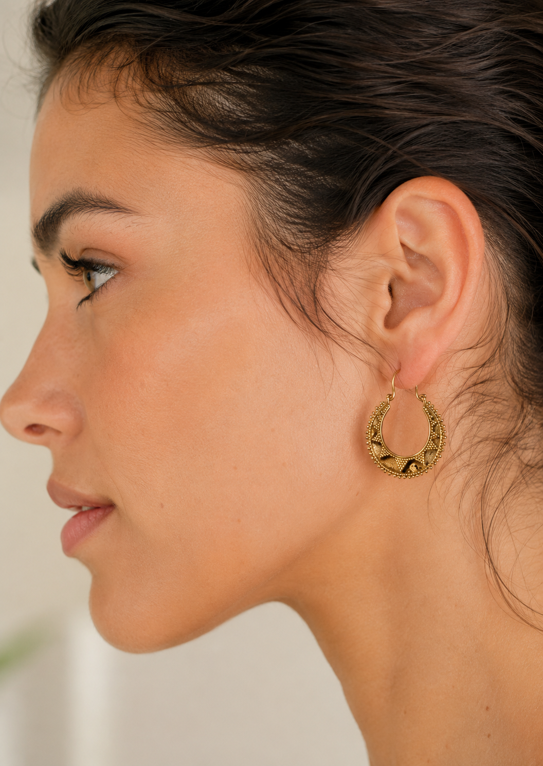Close up of a woman wearing a softly rounded crescent hoop earring inspired by traditional Indian jewellery. The raised bead edging and textured triangle detailing give it a lovely handcrafted feel, adding interest and shine.