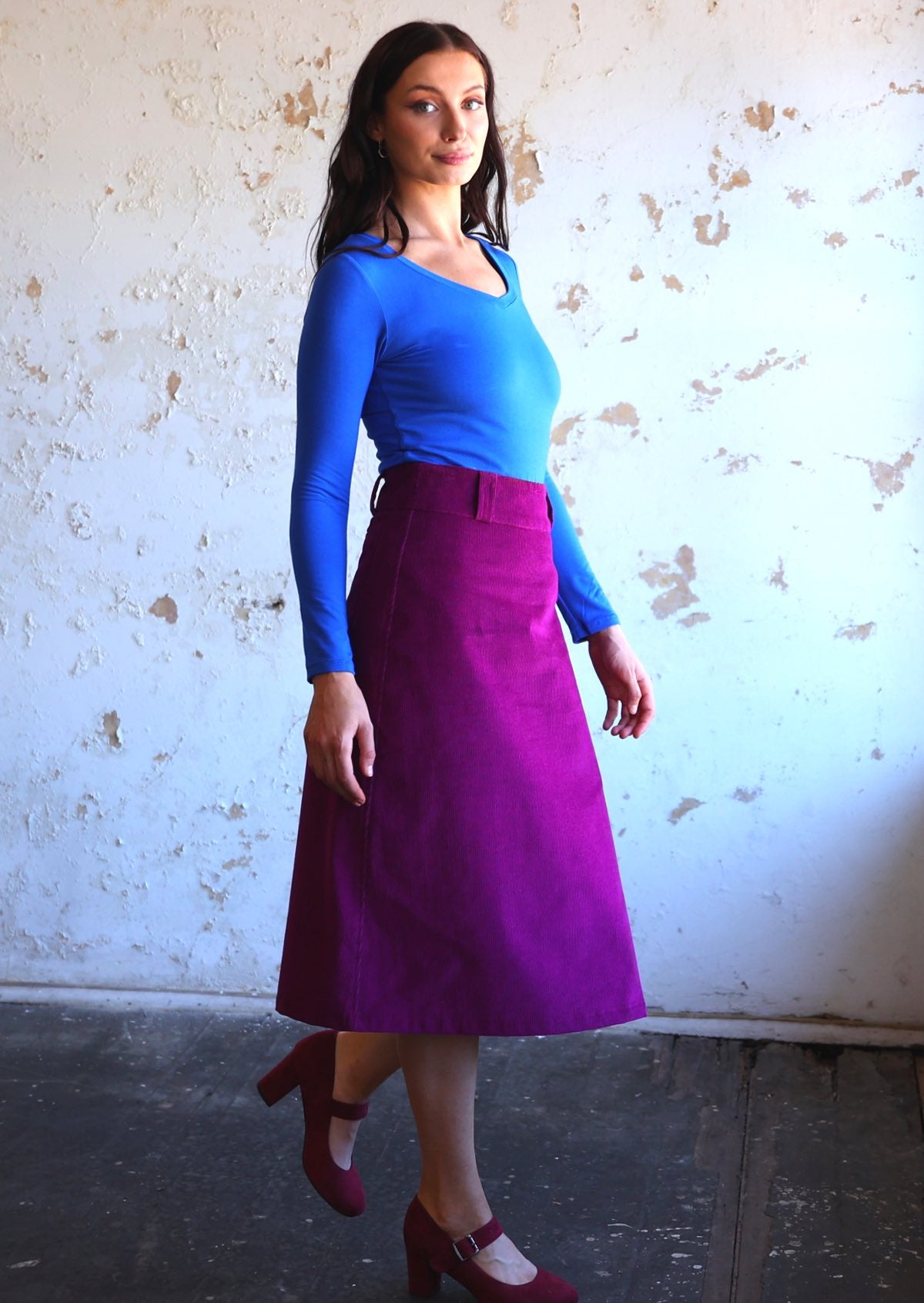 woman wearing purple corduroy aline skirt  with belt loops with bright blue long sleeve top