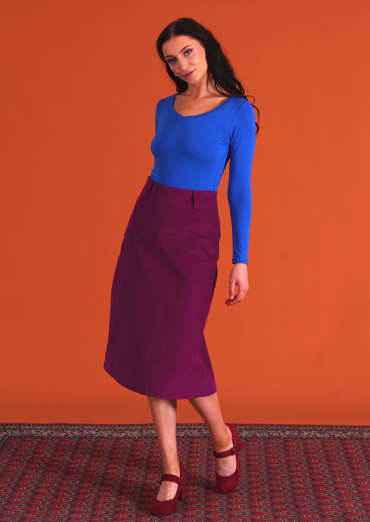 woman wearing purple corduroy aline skirt  with belt loops with bright blue v-neck long sleeve top