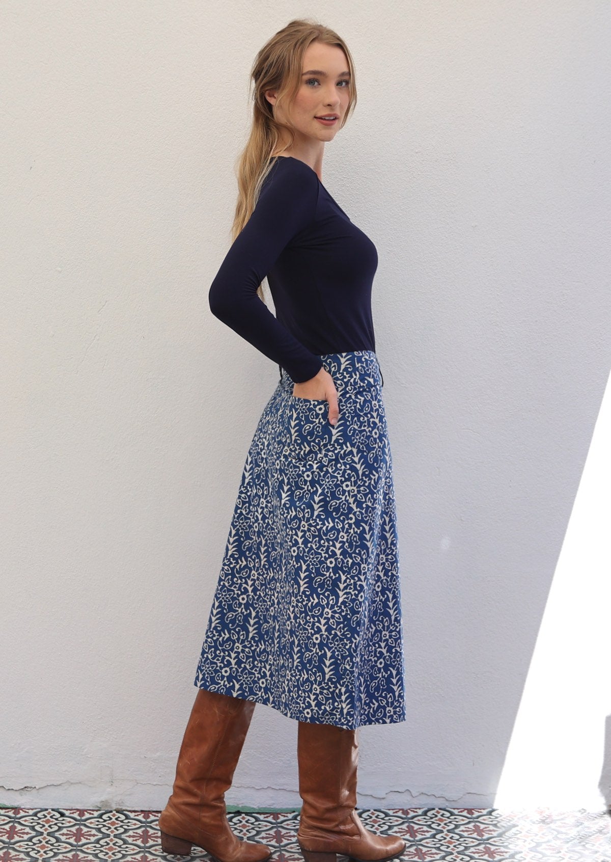 Woman stands sideways in cotton A-line skirt with belt loops and side zip, with her hand in back pocket