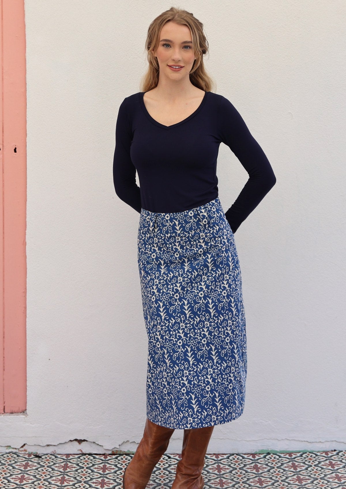 Woman poses in a blue based floral print cotton midi length A-line skirt with a long sleeve stretch rayon top in navy blue
