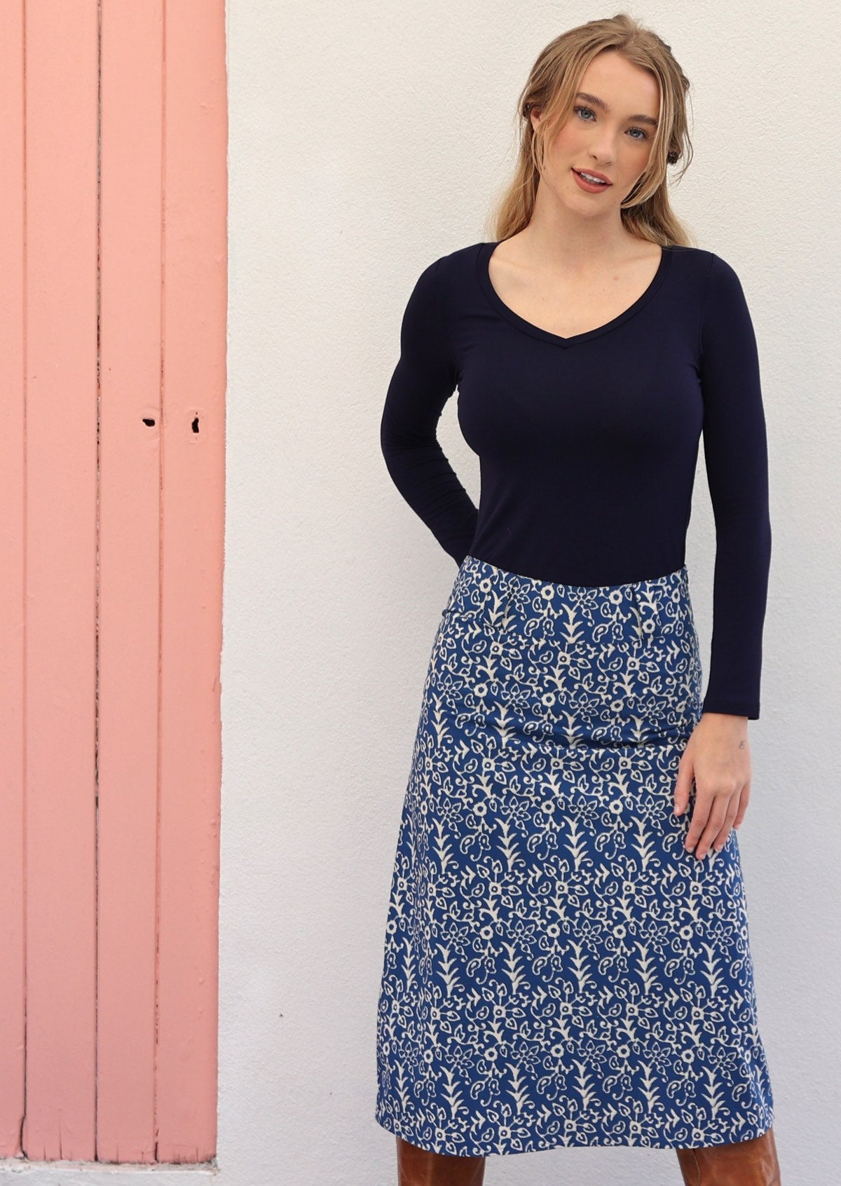 Model poses in cotton A-line midi length skirt in blue based floral print, paired with a navy blue long sleeve top