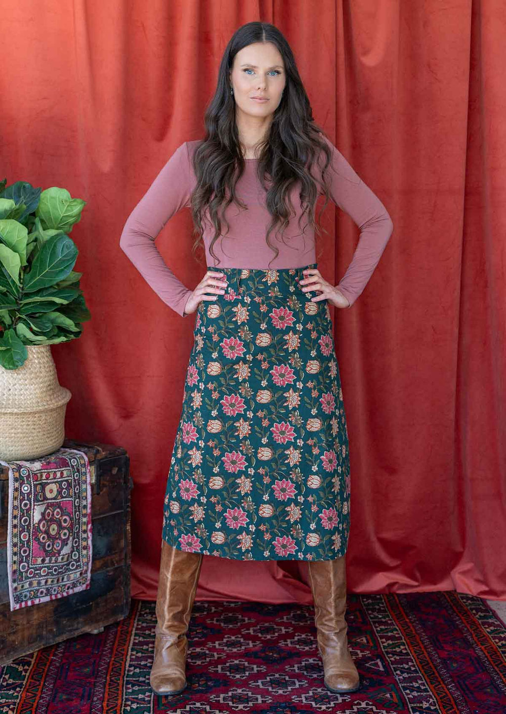 Model poses in cotton A-line midi length skirt in deep green based floral print, paired with a dusty rose long sleeve top.