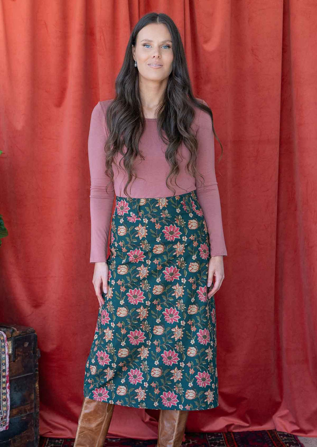 Model poses in dark green based floral print cotton midi length A-line skirt with pink, orange and cream floral print.