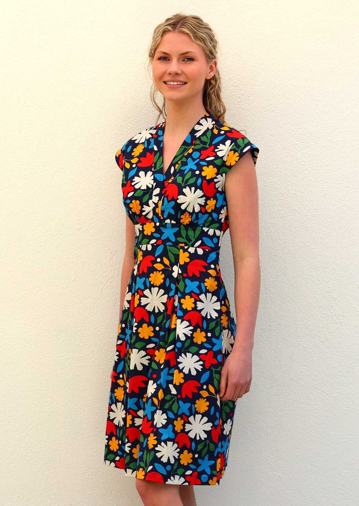 Model standing slightly to the side wearing 100 percent cotton dark navy blue base and bright abstract floral print cotton retro dress