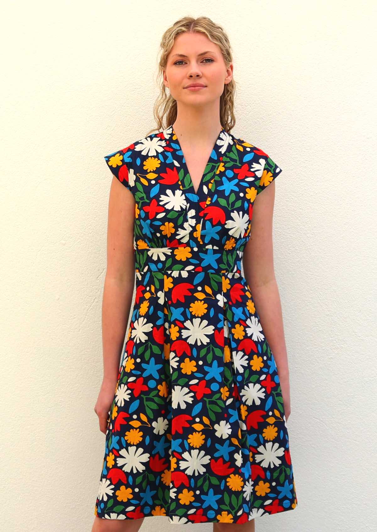Model standing wearing 100 percent cotton dark navy blue base with bright abstract floral print cotton retro knee length dress, with cap sleeves