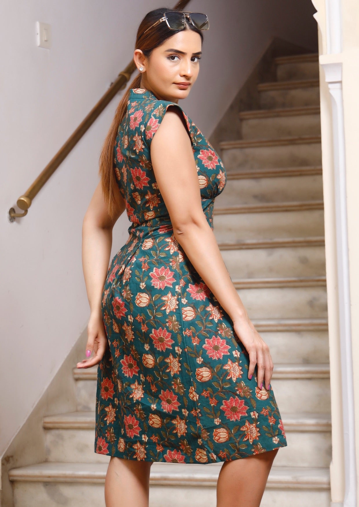 Side pose of model in pinkish bold floral printed, retro style dress with cap sleeves and fitted waist