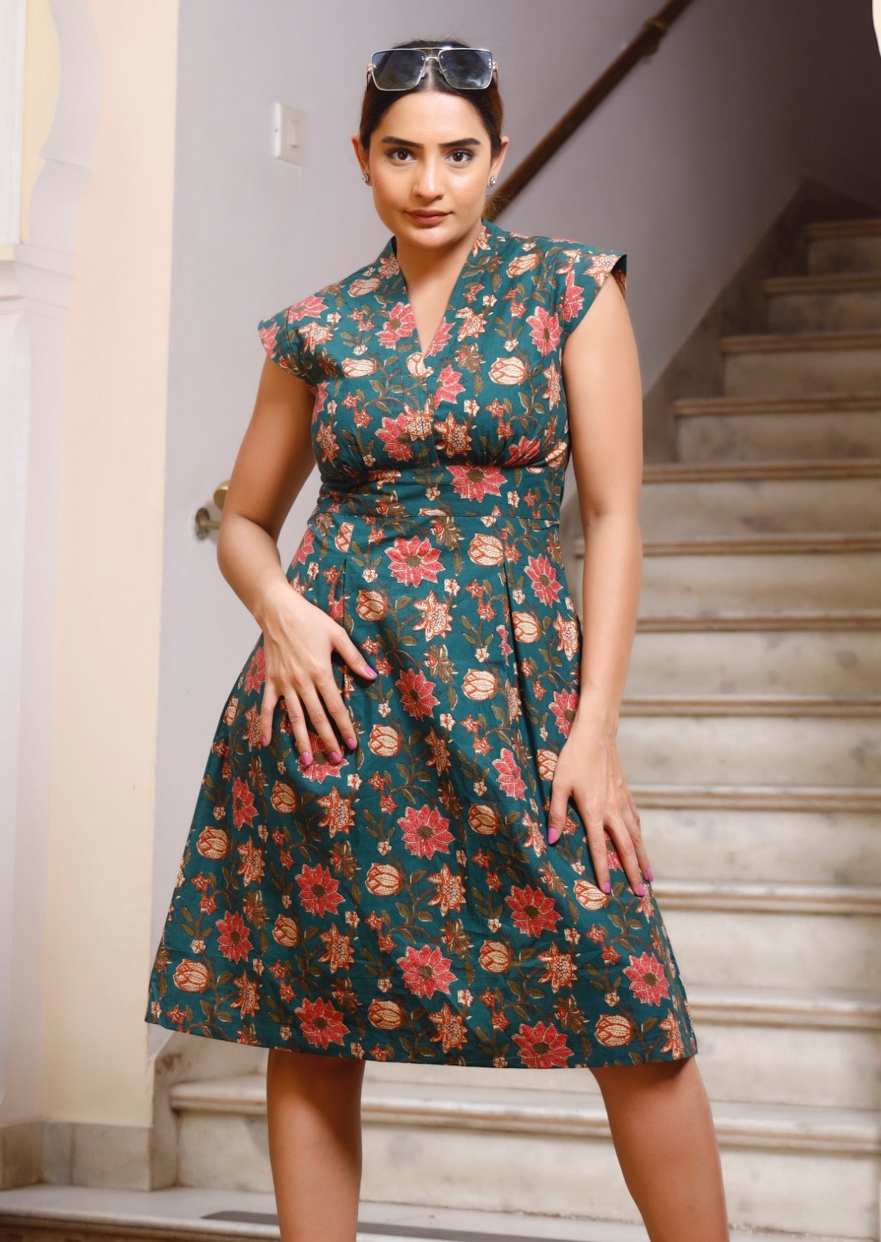 Model wears green based floral printed cotton dress with cap sleeves, A line skirt and box pleats at the waist.