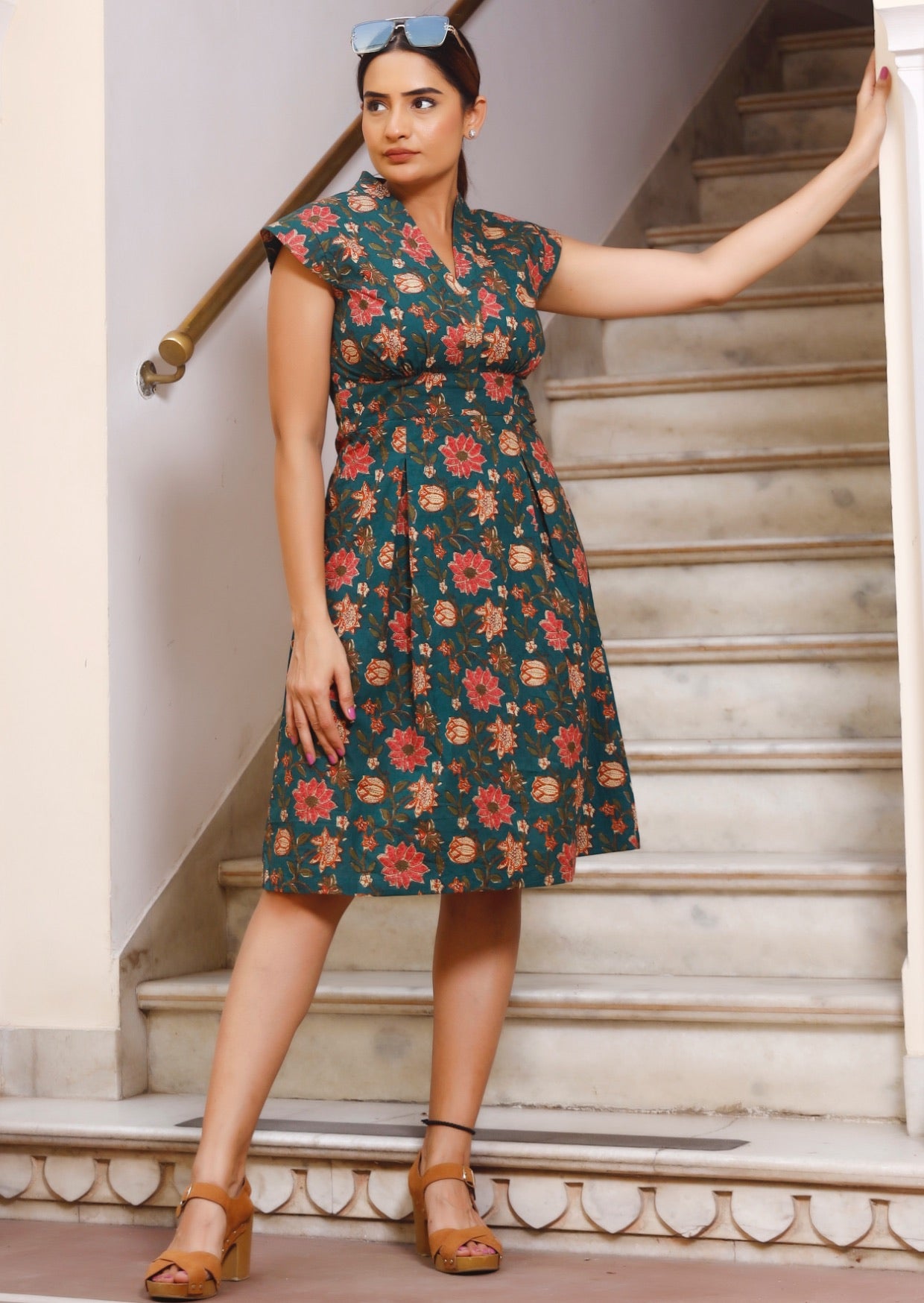 Model standing in front of stairs wears 100% cotton retro style, knee length dress with fitted waist, cap sleeves and V neckline.