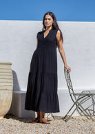 Woman wearing a long black dress standing against a white wall with a blue sky.