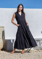 Woman wearing a black maxi dress standing against a white wall with blue sky.