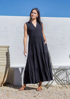 Woman wearing a black dress sundress standing against a white wall with blue sky.