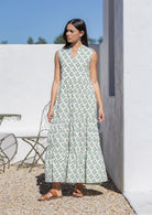 Woman wearing a sleeveless white cotton maxi dress with a floral pattern outdoors.