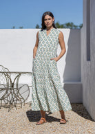 Woman wearing a sleeveless floral cotton maxi dress standing outdoors against a white wall.