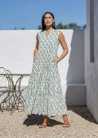 Woman in a floral cotton maxi dress standing outdoors with a white wall and bench in the background.