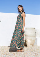 Woman wearing a 100 cotton floral maxi dress standing against a white wall with a blue sky.